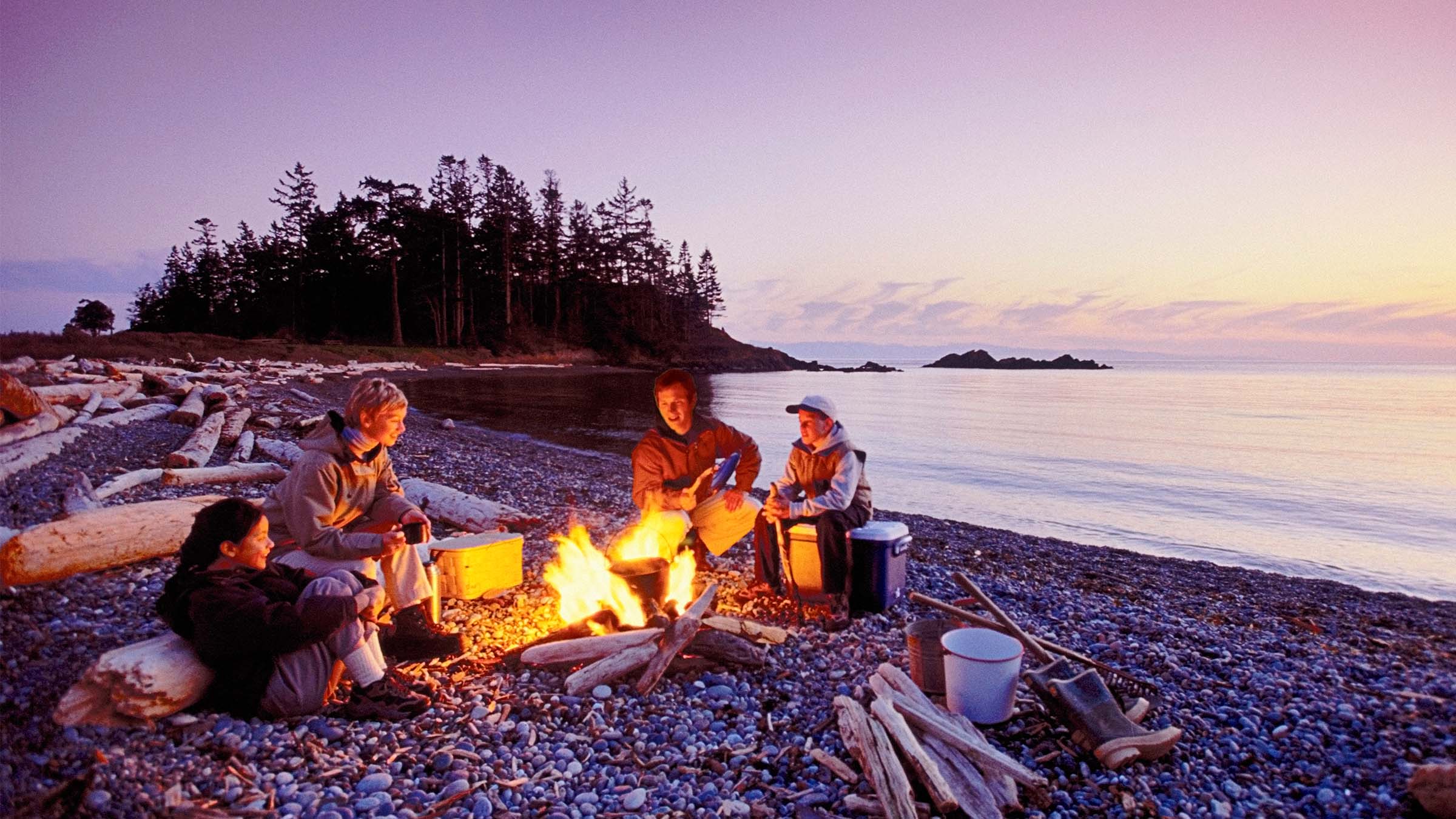 Four people sitting around a campfire on the beach