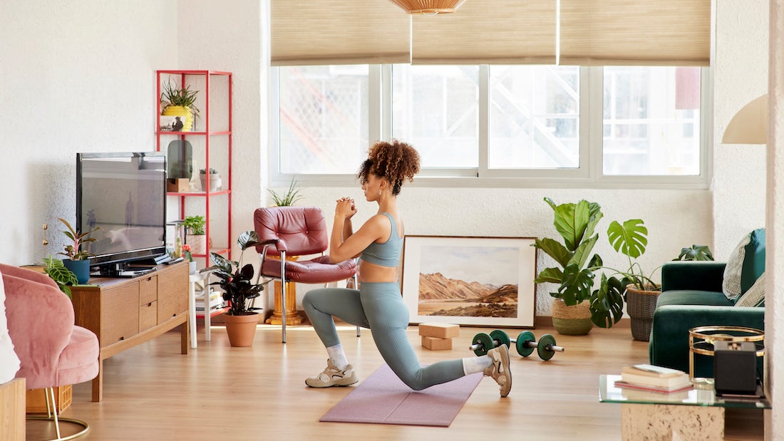 Full length of woman doing lunges while watching online yoga class. Female is wearing sports clothing in living room