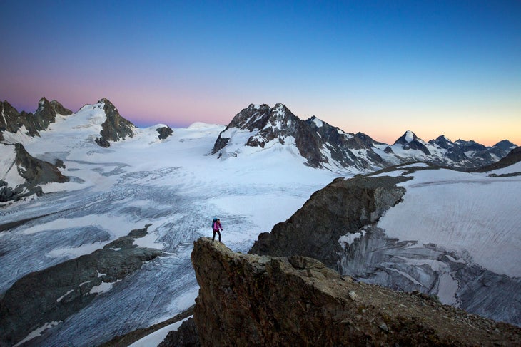 Vignette Hut A hiker at sunset high above glacier covered mountains using a headlamp while walking to the Vignette Hut on the third day of the Chamonix to Zermatt…