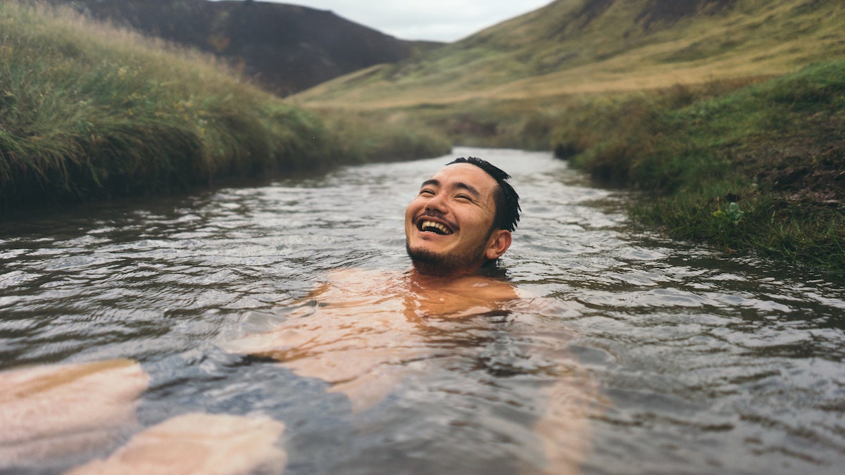 Man soaking in beautiful natural hot spring in Iceland surrounded by mountains and nature