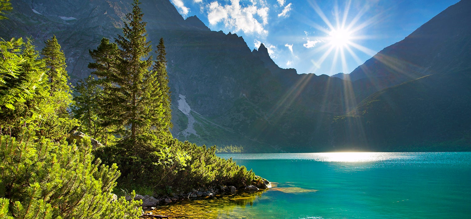 "Image of glacial blue alpine lake water in the Polish Tatra Mountains while the sun shines in a starburst."