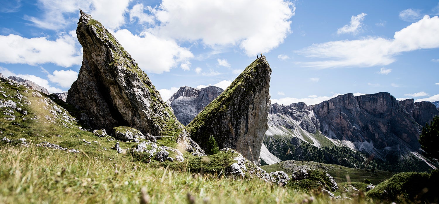 "Foreground features out of focus grass. Two large boulders with tiny people on top of them are featured toward the left of the image in the&hellip;"