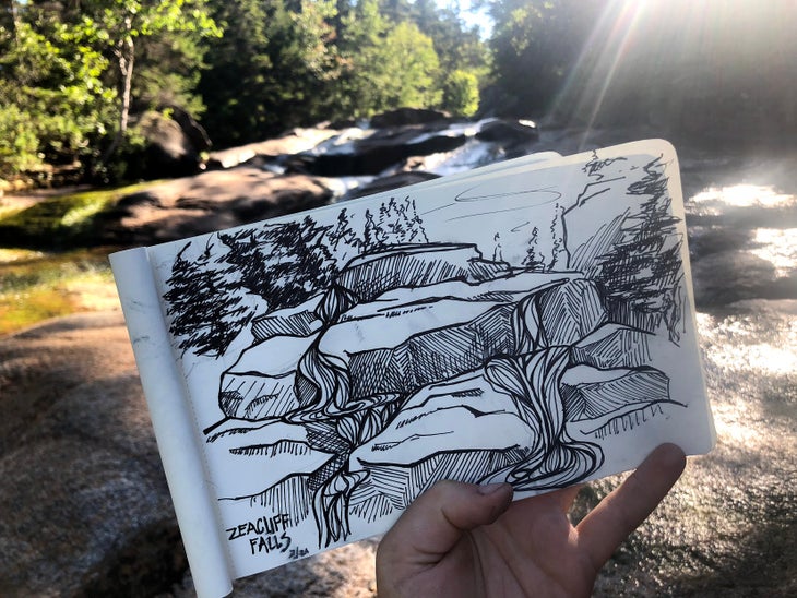 Zealand Falls Sketchbook - Heidi Nisbett Sketch of Zeacliff Falls held in a hand in front of the location. Water rushes over rocks in the background.
