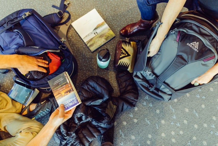 Two people put things away in their Gregory backpacks on an airport floor.