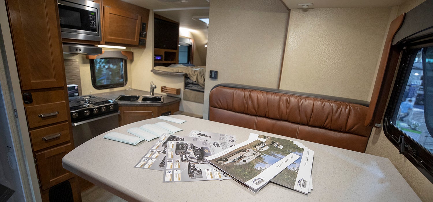 "Interior of the Lance RV. Kitchen table and mini kitchen is in sight. There is a bed in the distant background."