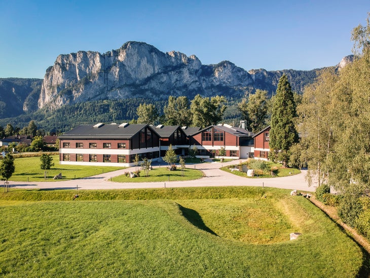 Komperdell's headquarters is a red brick building sitting with grass in the foreground and a rocky cliff behind it. Clear blue skies above in…
