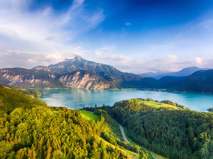 Austrian hills covered in evergreen trees surrounding a turquoise lake with rocky mountains in the background.