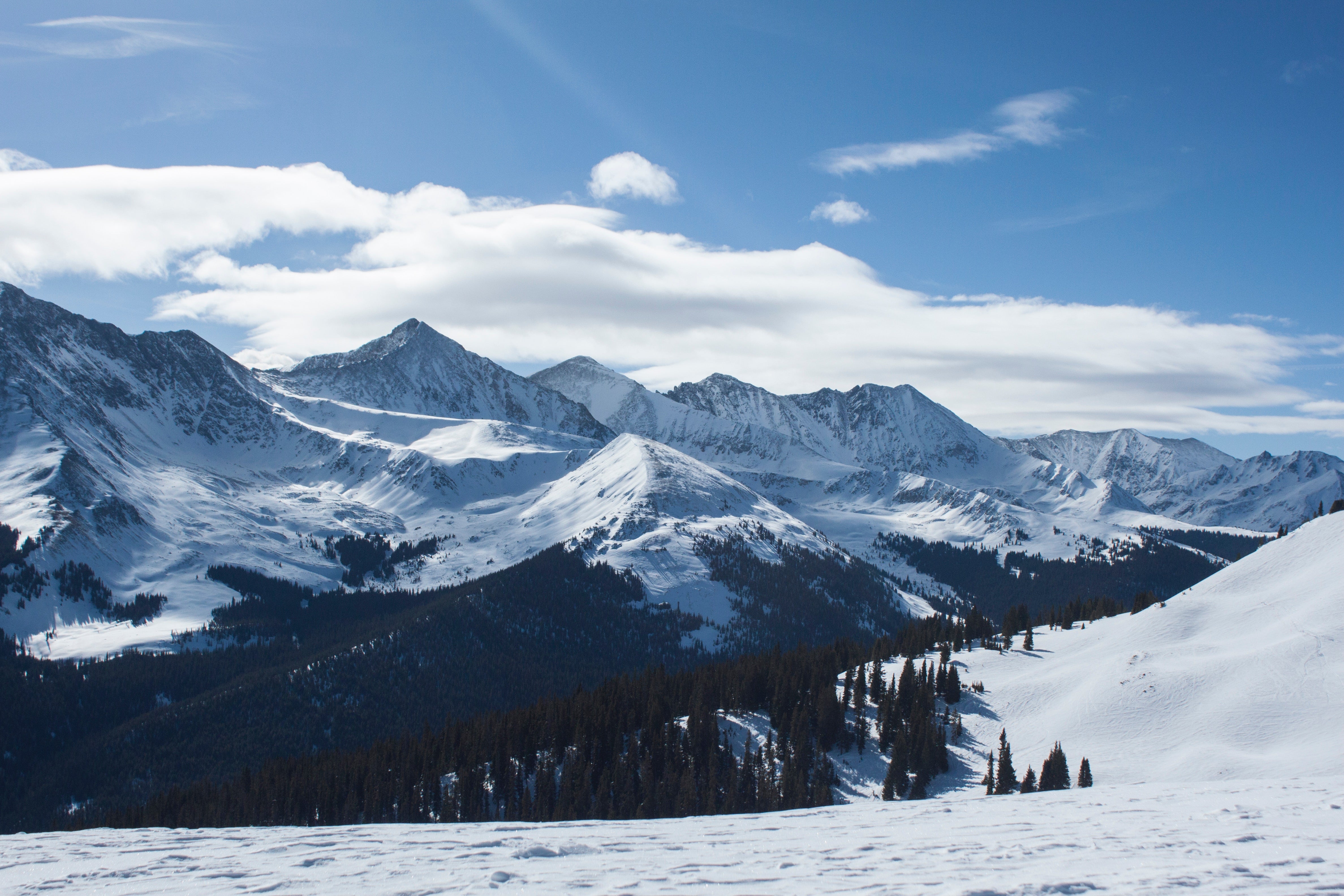 "Views from Copper Mountain, Colorado. Snow-covered mountains sit against a partly cloudy and blue sky."