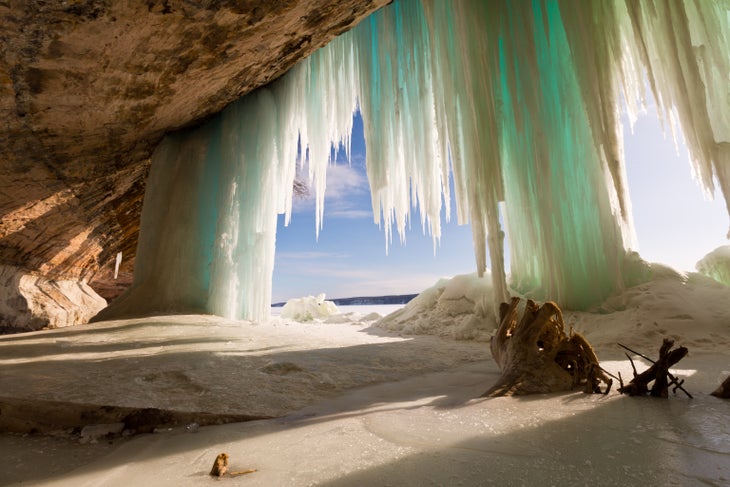 iStock-523879824_GrandIsland_PicturedRocks_Michigan Icicles hang over the edge of a cave in Pictured Rocks Michigan. Photo is from the inside of the cave looking out as the sun shines through. A stump…