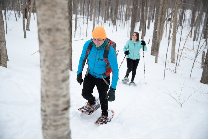 arab2 A white man and white woman wear blue and turquoise jackets and black pants as they snowshoe through the bare trees of the Adirondack Mountains.