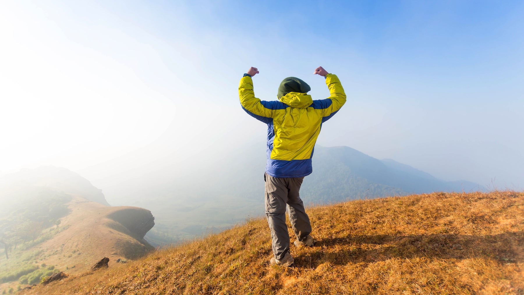 Full Length Rear View Of A Man flexing back muscles on a mountain.