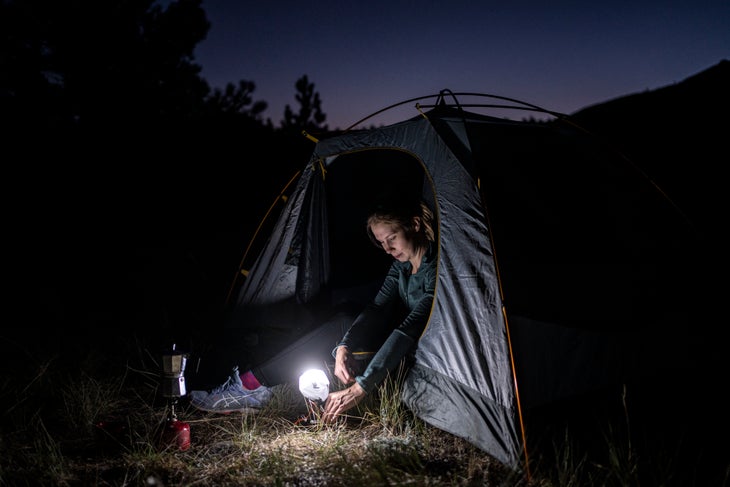 Petzl_strange_09_lantern Woman sitting in tent doorway with headlamp lantern.