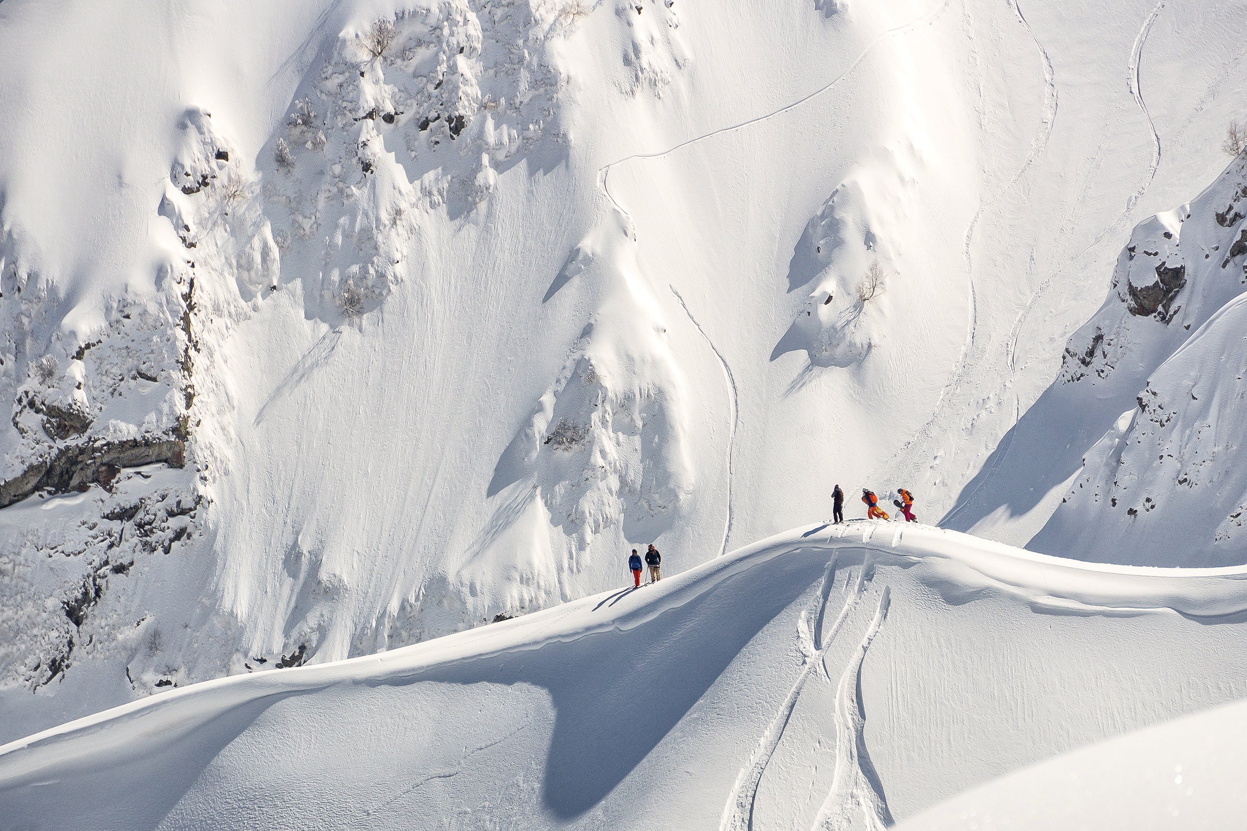 "Five skier standing on a snowy slope in front of a steep mountainside"
