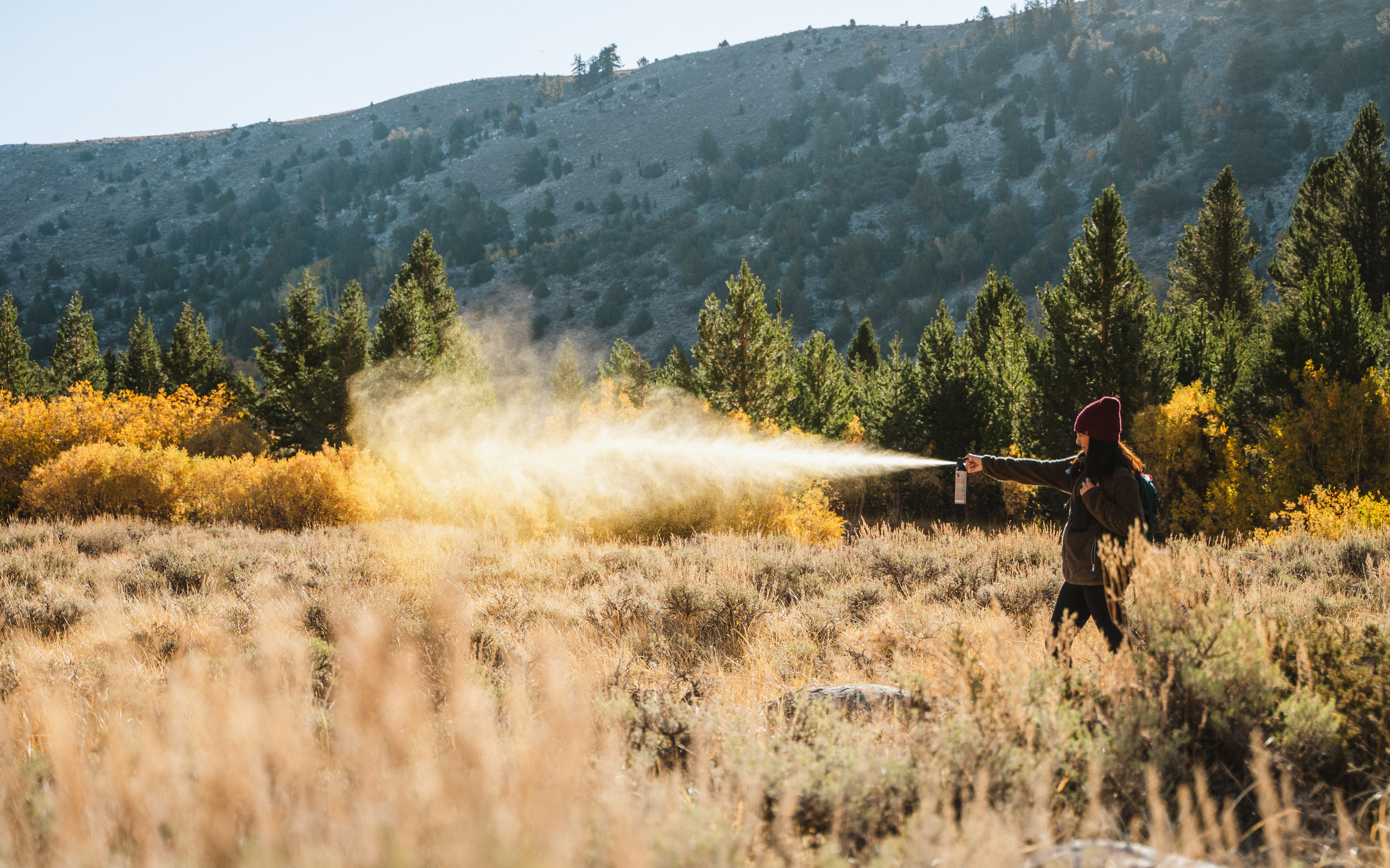 Woman setting off bear spray in the brush near a forest