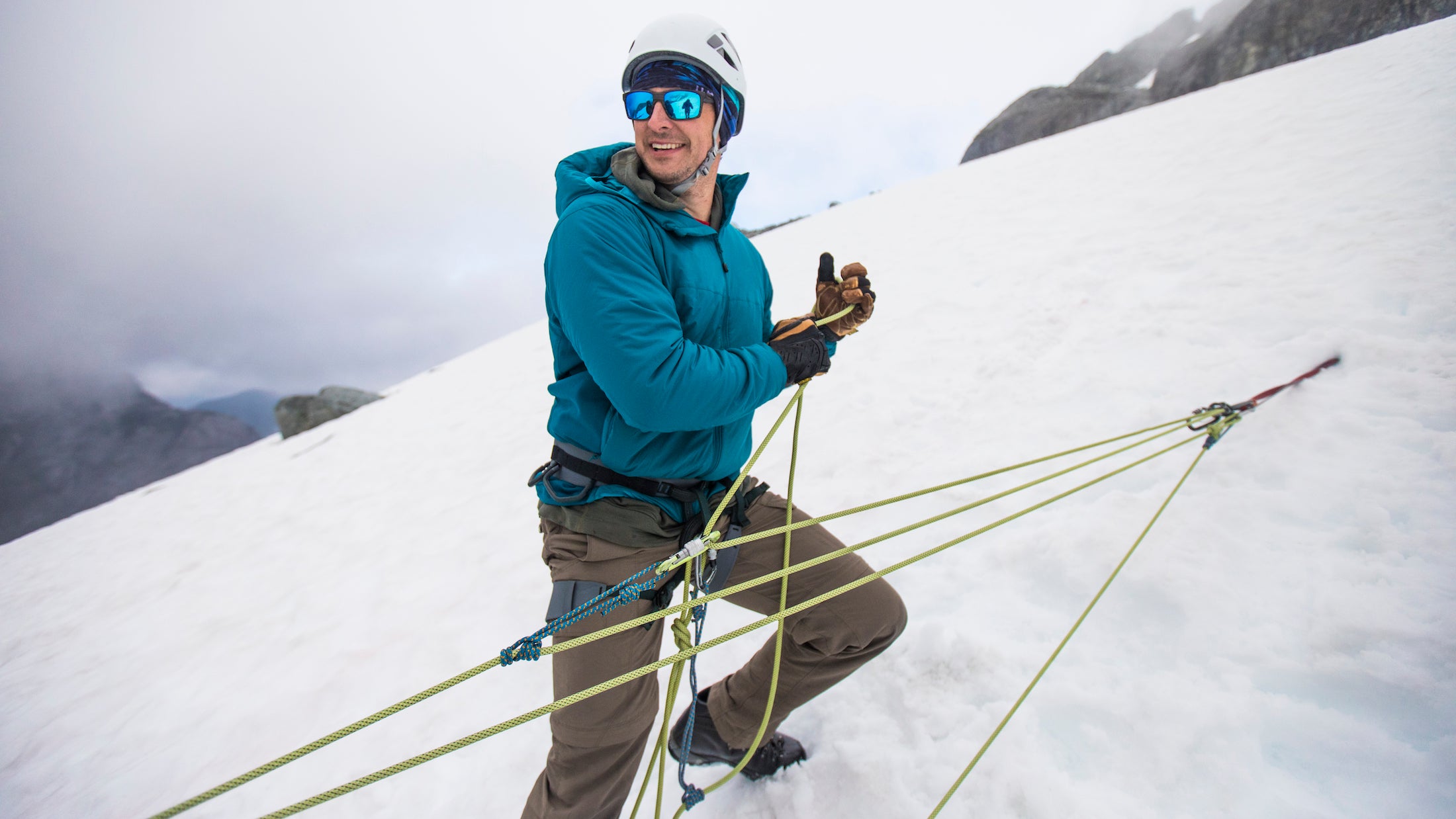 mountaineer climbs steep mountain with snow anchor