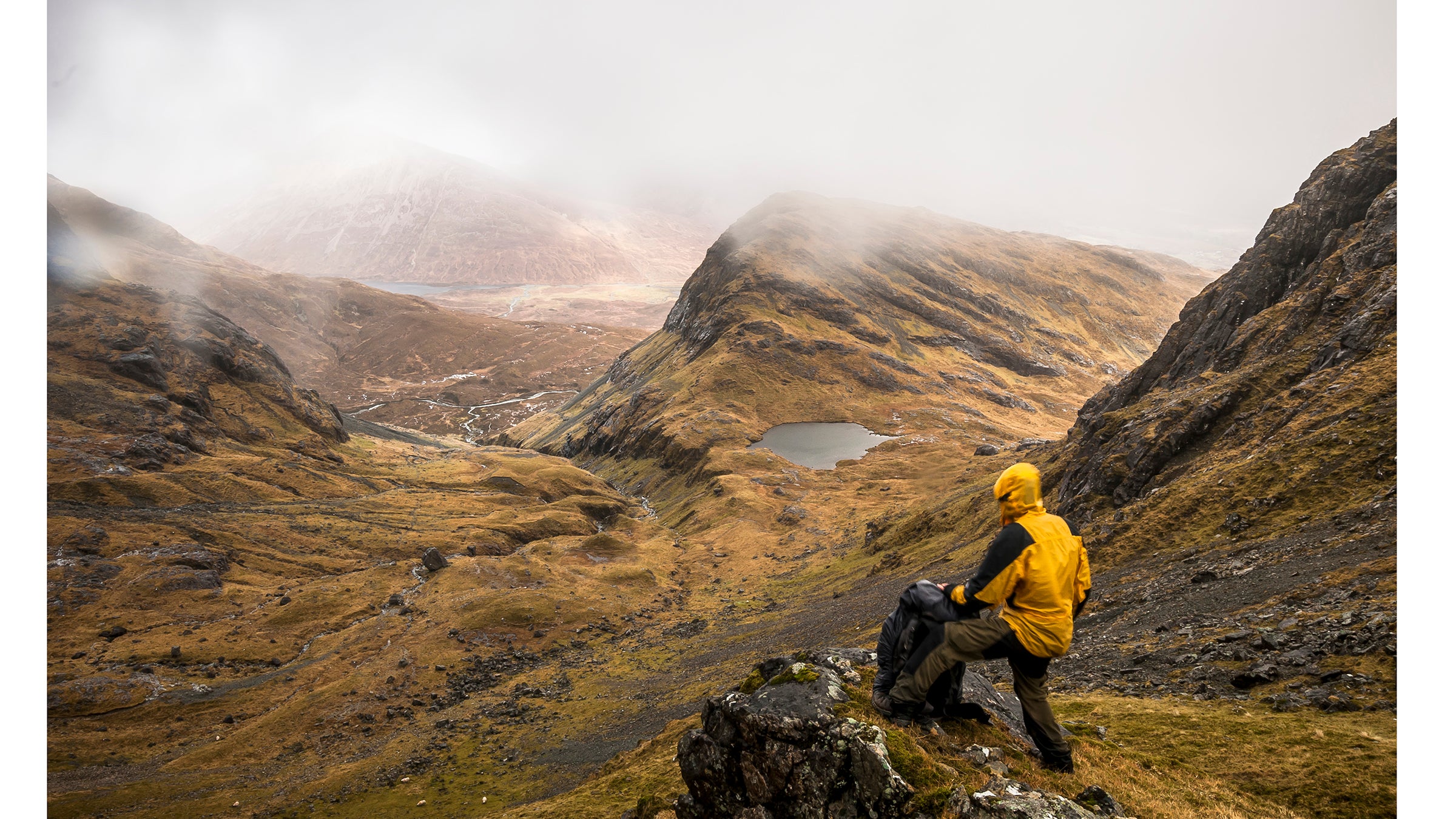 A hiker surveys the landscape as rain and fog move in.