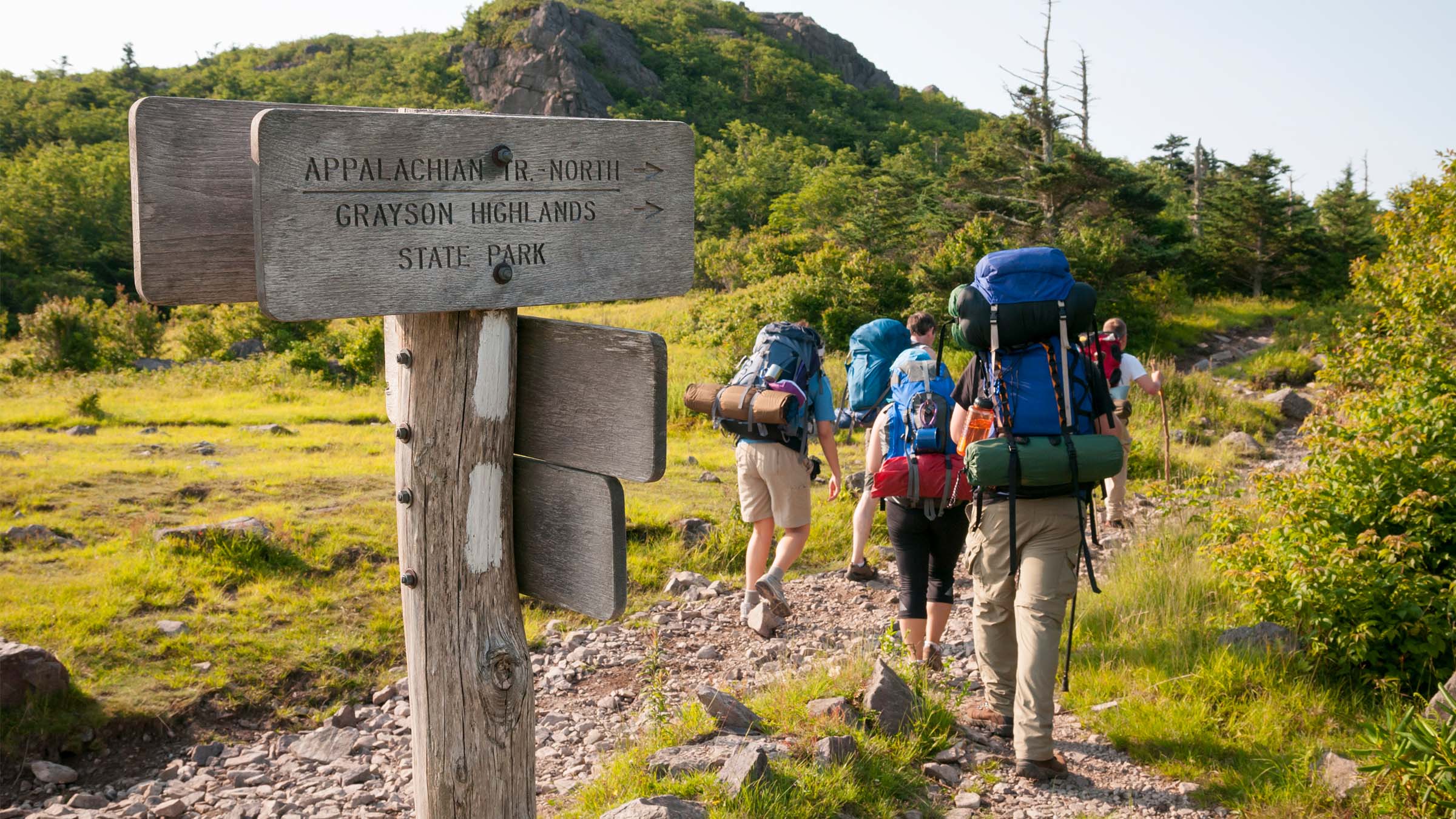 Backpackers hike by a trail sign on the Appalachian Trail.