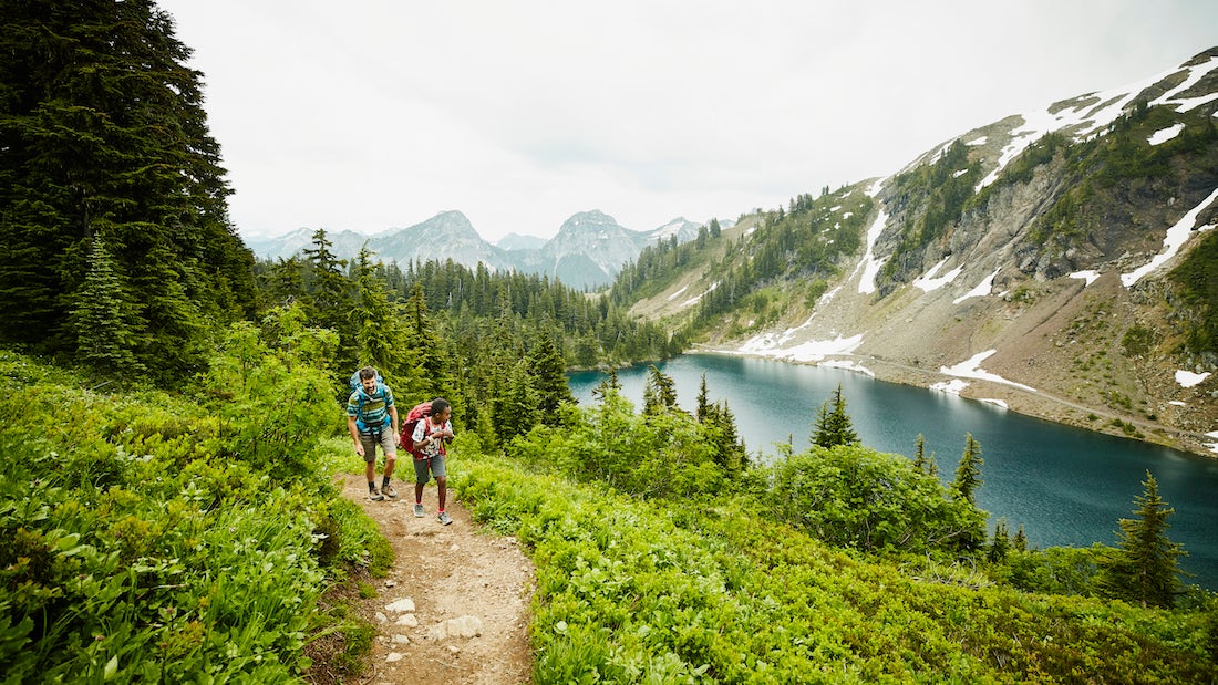 Father and son hiking on mountain trail above alpine lake