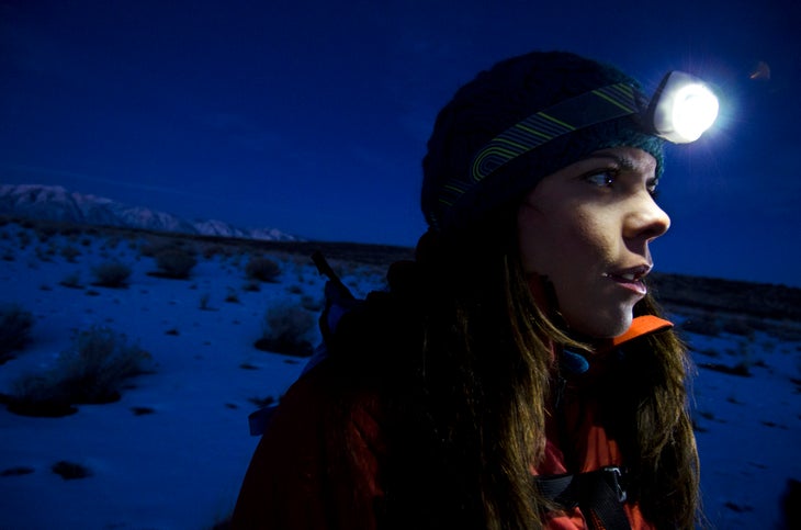 A close up shot of a female hiker wearing a headlamp. It's dark.