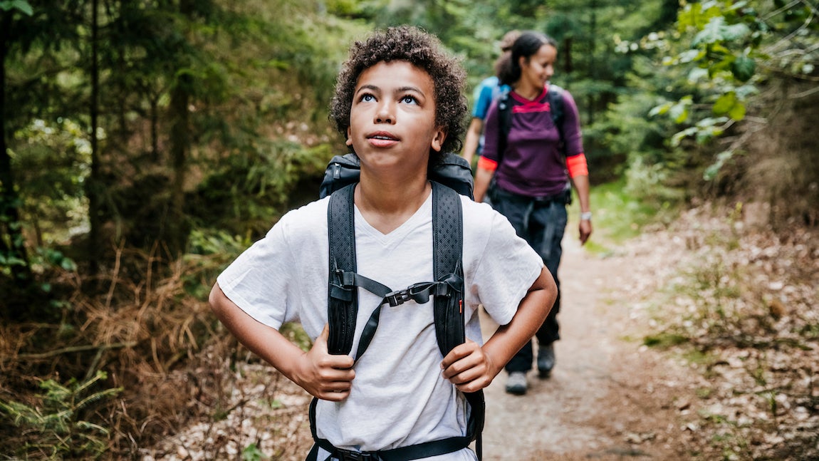 A young boy looking around and taking in the view while out hiking together with his family.