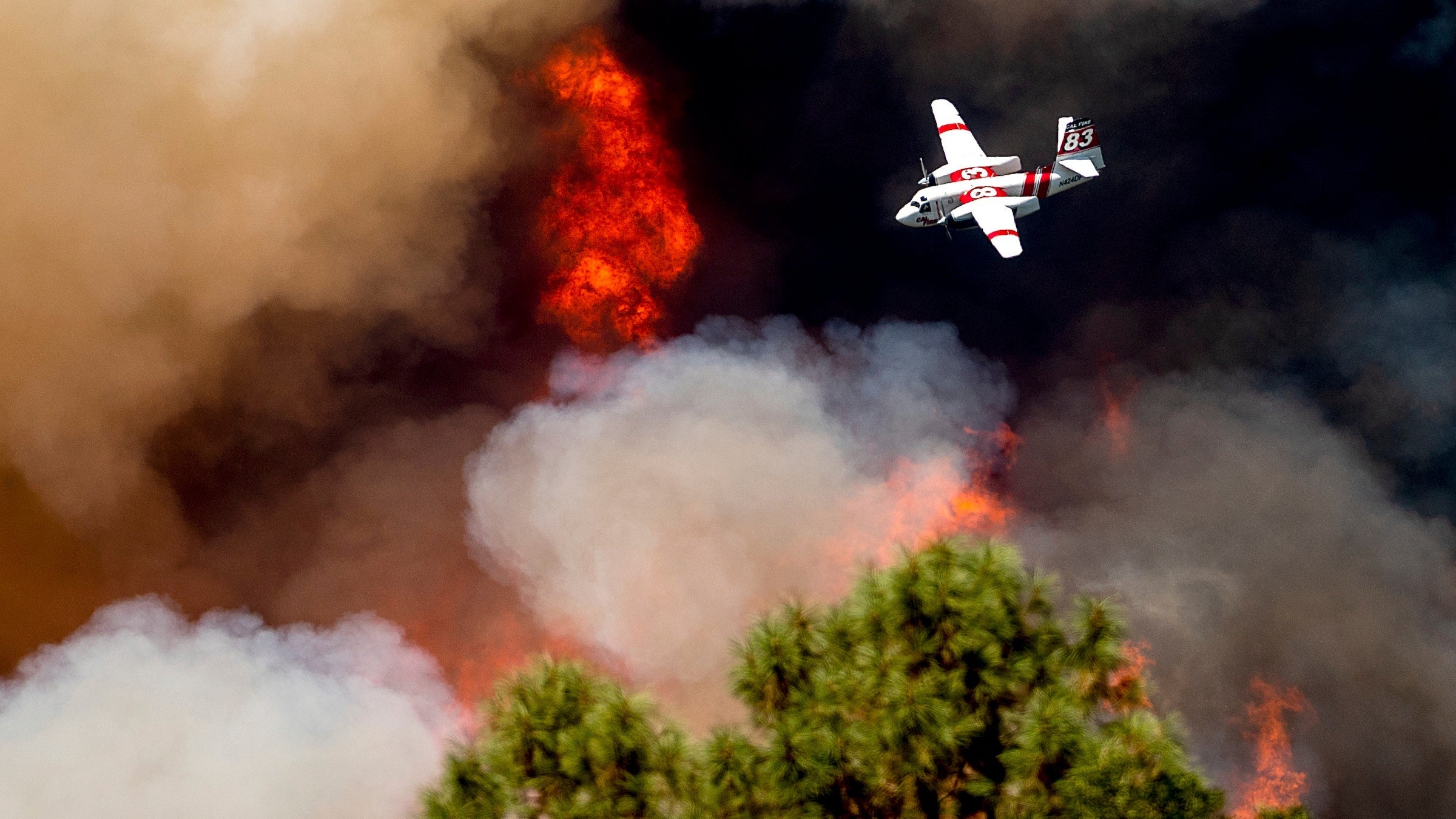 An air tanker flies past flames while battling the Oak Fire in Mariposa County, California, on Sunday, July 24, 2022