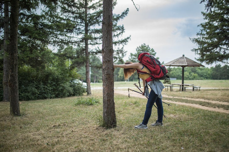 female hiker leaning against tree, catching breath