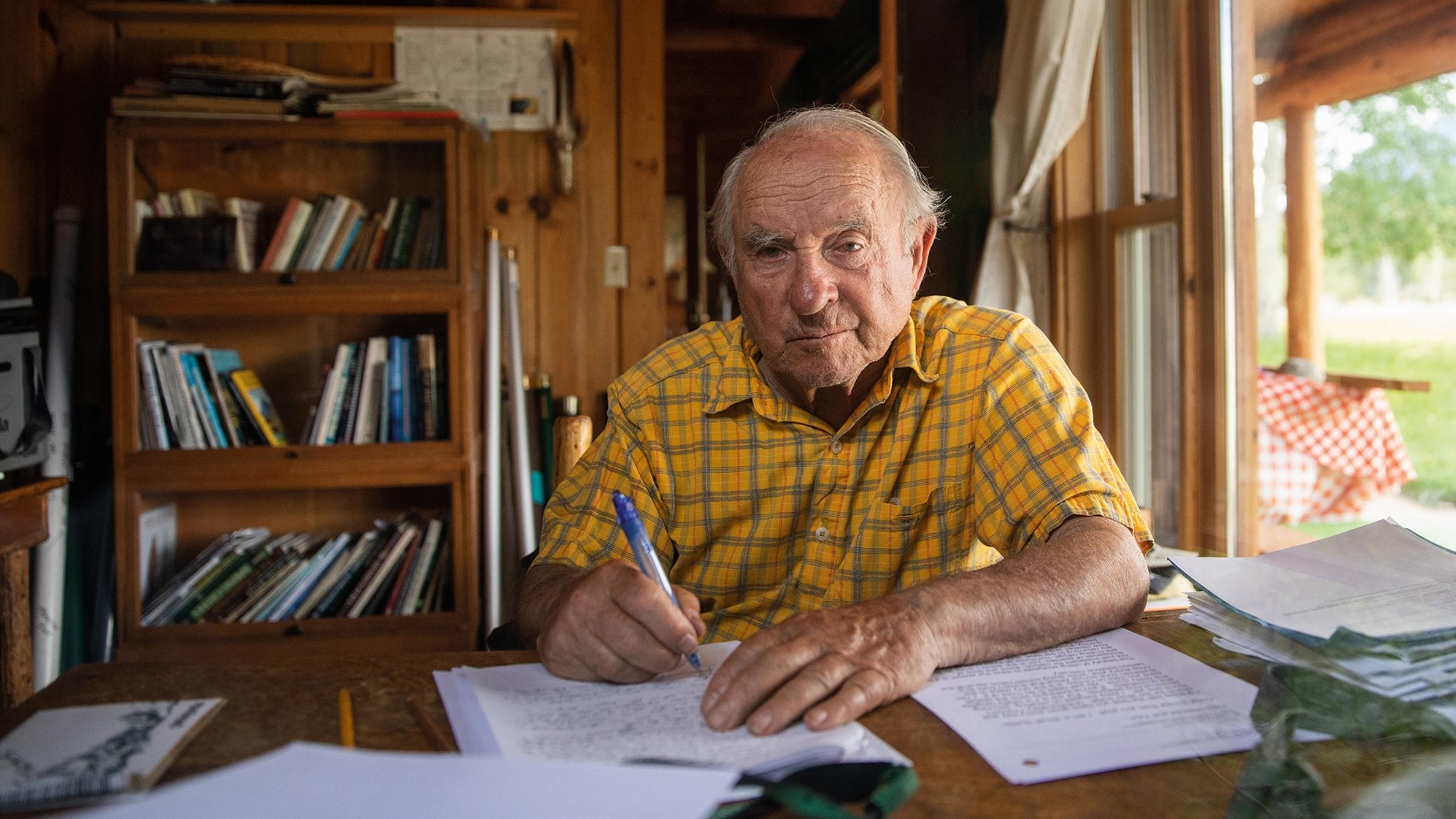 Man in yellow shirt sitting at a desk writing