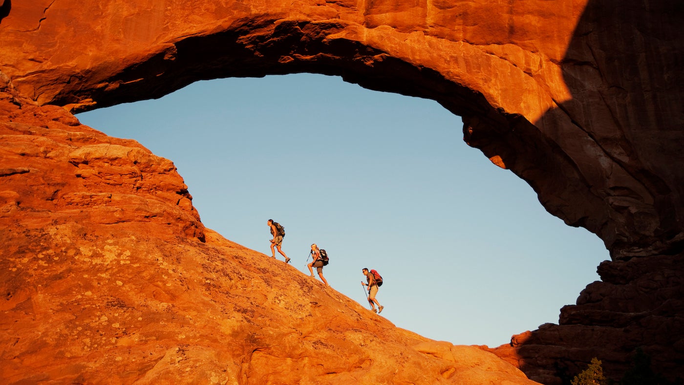 Three hikers explore the North Window at sunrise in Arches National Park.