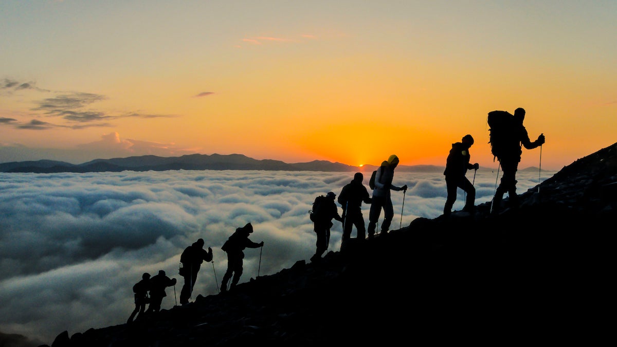Silhouettes of hikers climbing the mountain at sunset