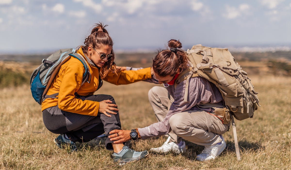 man on a hike examines a girl's leg injury