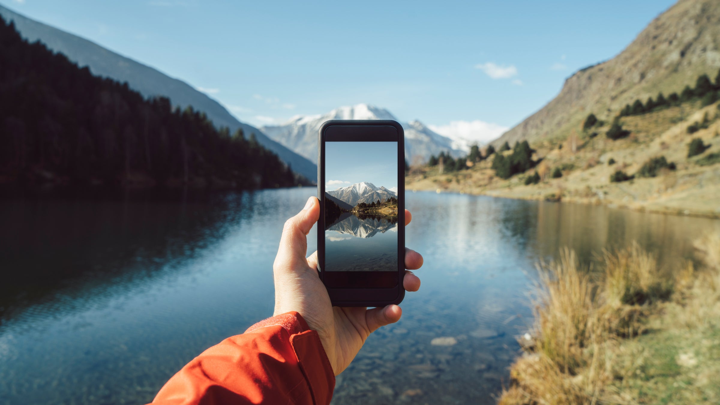 POV of hiker taking a phone photo of a mountain lake.