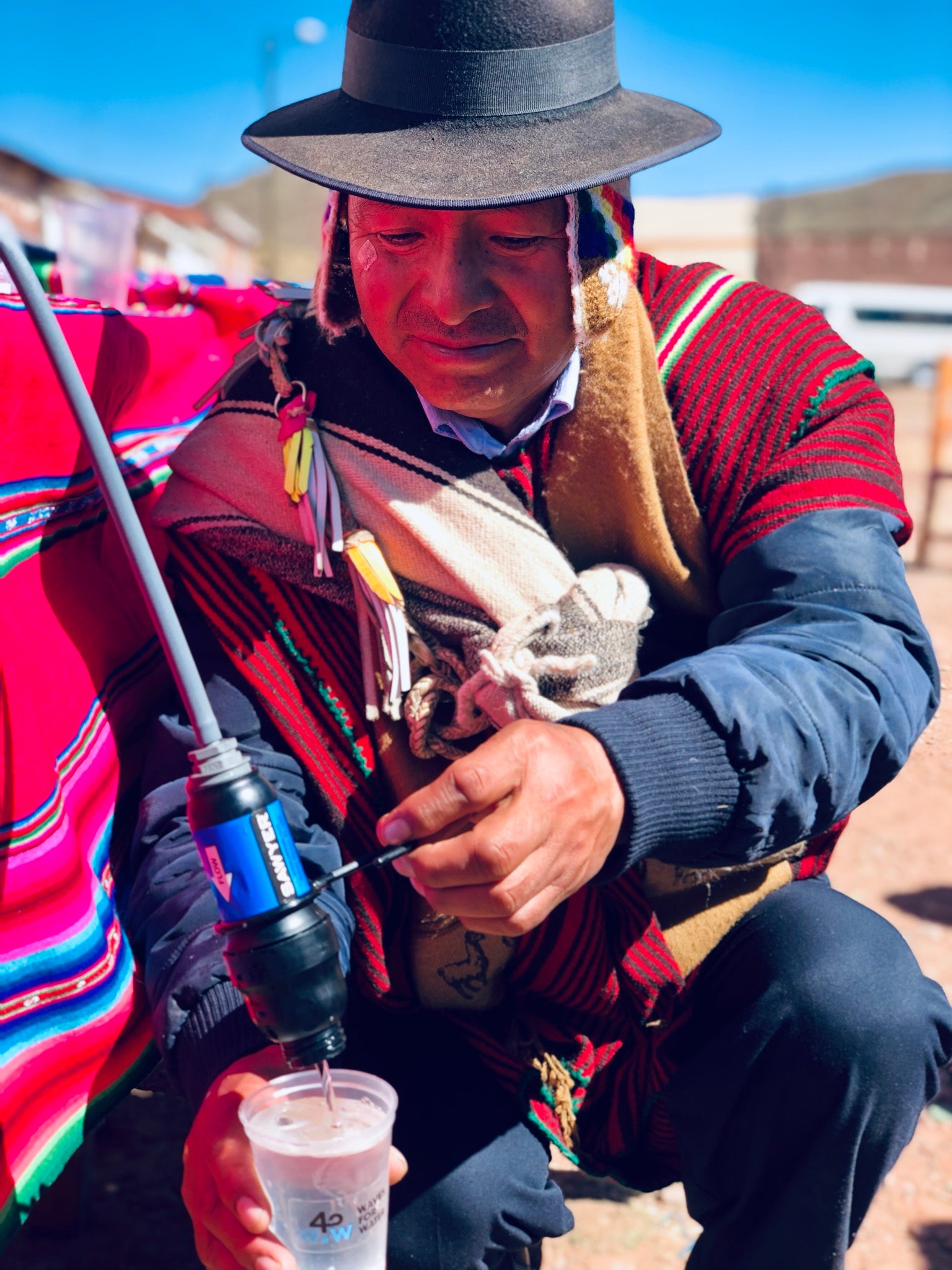Unknown Man in Bolivia pours water from a bucket with a Sawyer water filter.